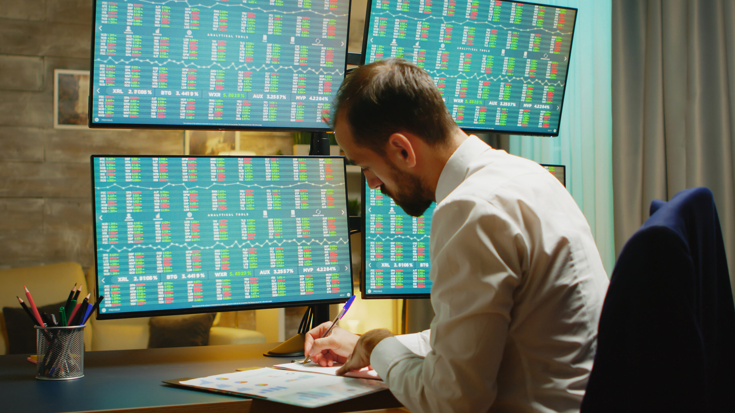 bearded businessman taking notes while checking stock market from home office 1 scaled